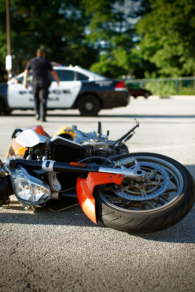 Injured motorcyclist sitting beside a crashed motorcycle on a Florida road while calling for legal help after an accident.