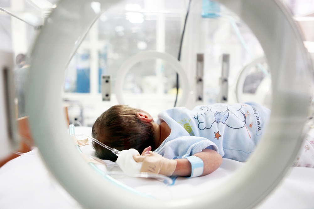 Newborn baby in a hospital crib recovering from a birth injury, with medical staff nearby.